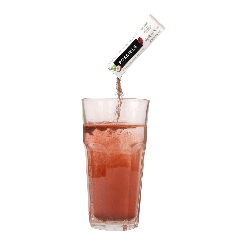 Action shot of a Possible electrolyte powder being poured into a glass of pinkish-red drink. Emphasizes easy mixing and refreshing hydration